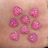 Eine Hand hält mehrere rosa herzförmige Ornamente, die mit glitzernden Strasssteinen überzogen sind.