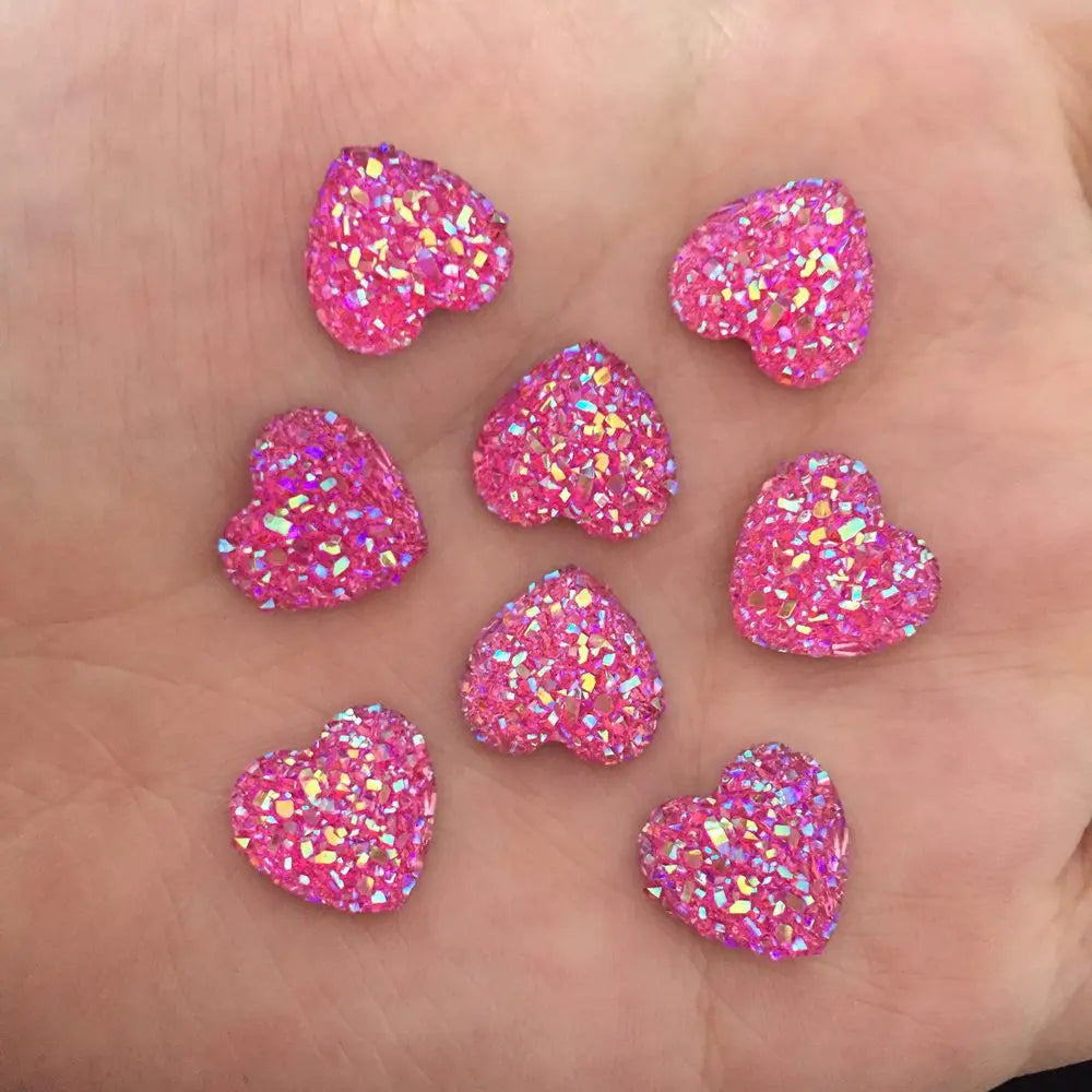 Eine Hand hält mehrere rosa herzförmige Ornamente, die mit glitzernden Strasssteinen überzogen sind.