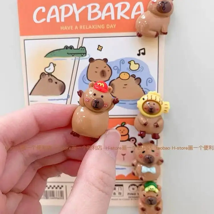 A hand holds a small brown guinea pig figure, part of an adorable refrigerator magnet set featuring various animals.