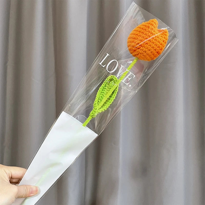A clear plastic sleeve containing a handmade orange crochet tulip flower and a green stem, suitable for home decor or gifting