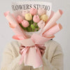 A bouquet of handmade crochet tulip flowers in shades of pink and yellow, wrapped in light pink paper.