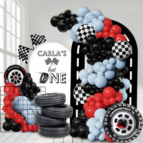 Set de arco de globos negro, rojo y azul junto a neumáticos apilados.