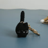 A black crocheted cat keychain pendant with a long tail and gold-toned hardware resting on a gray surface.