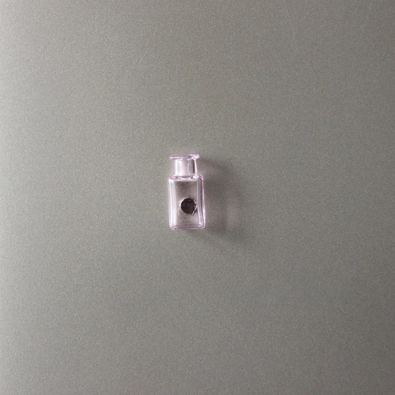 A small clear glass bottle with a stopper and a black disc is mounted on a muted green wall.