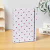 Álbum de scrapbooking de tela blanca con un patrón de pequeños corazones rojos sobre una superficie de madera.