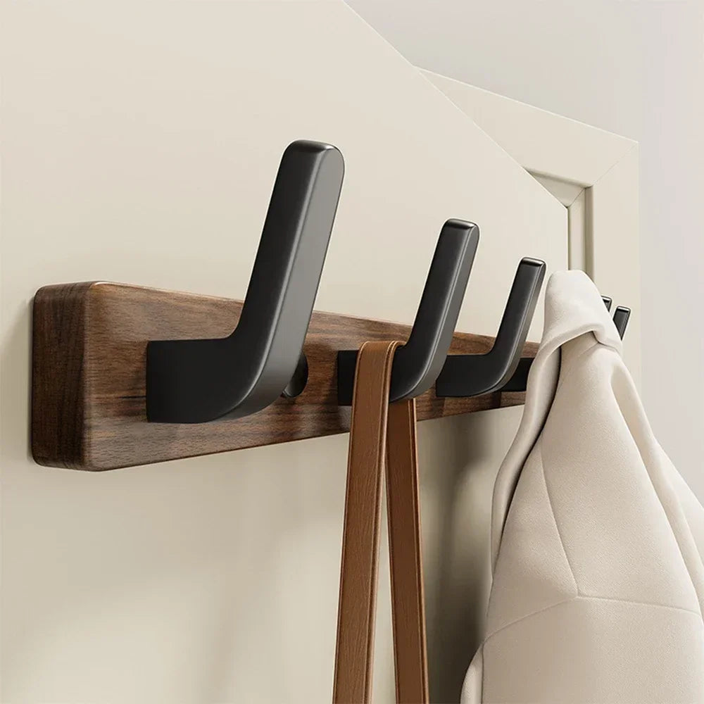 A walnut wood coat rack with eight black hooks and a storage shelf mounted on a light-colored wall.