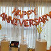 A decorative banner made of gold foil balloons spelling out Happy Anniversary strung across a window.