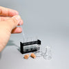 A hand is pipetting liquid into a set of miniature laboratory glassware for dollhouse or photography.