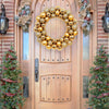 A golden silk Christmas ball wreath ornament displayed on a wooden door decorated with greenery and pine trees.