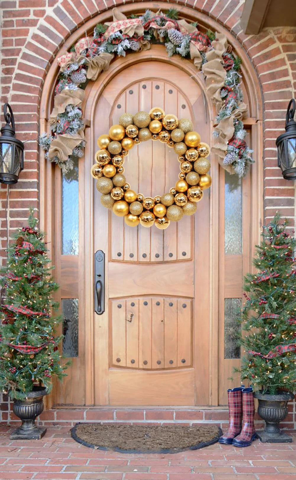 A golden silk Christmas ball wreath ornament displayed on a wooden door decorated with greenery and pine trees.