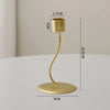 A gold-colored iron candle holder with a curved stem and a round base, shown against a light background.