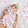 Una mano sostiene una pila de mini charmes de uñas de tortuga coloridos en rosa y blanco sobre un fondo blanco.