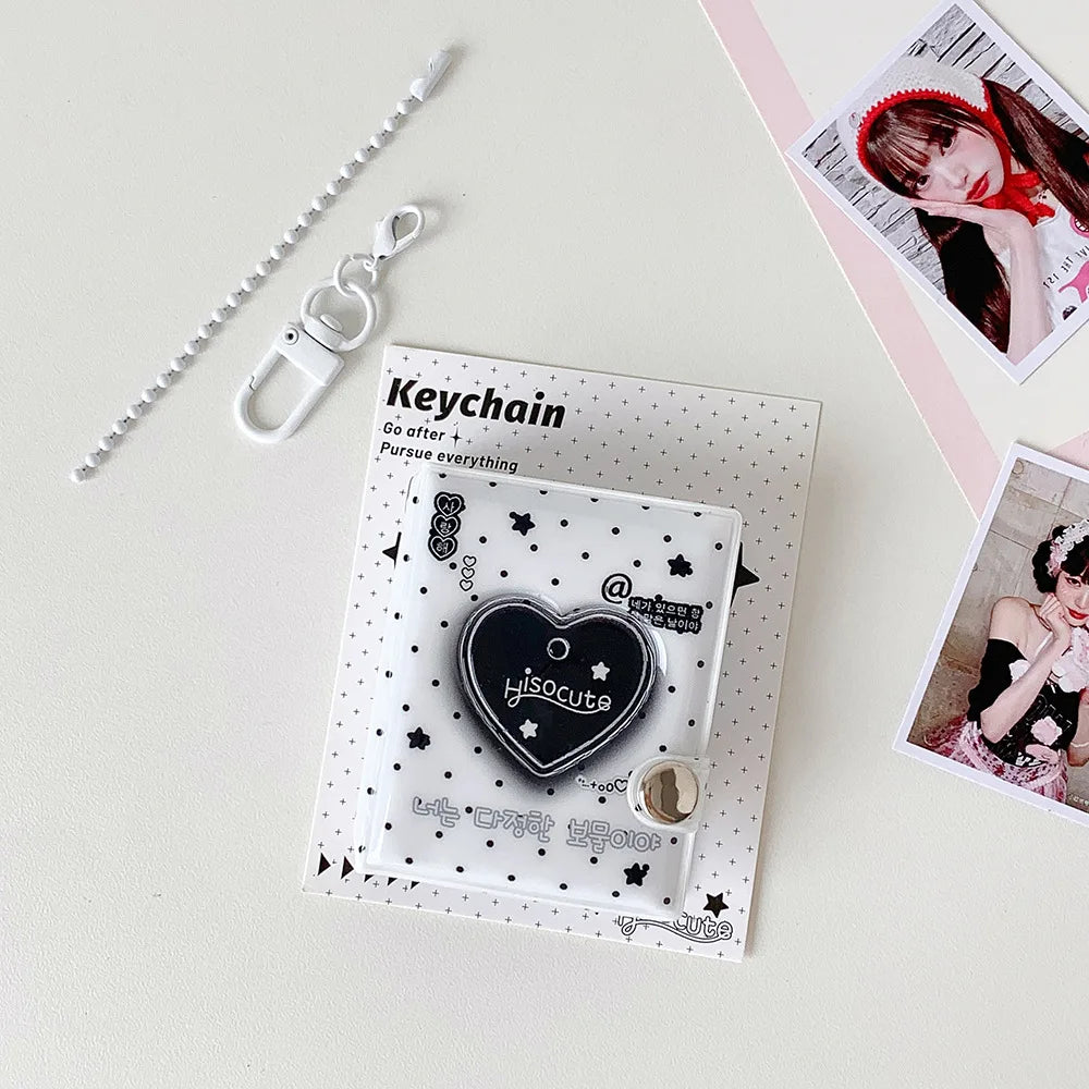 A clear plastic keychain featuring a black heart charm and text on a white card, displayed next to a silver chain.