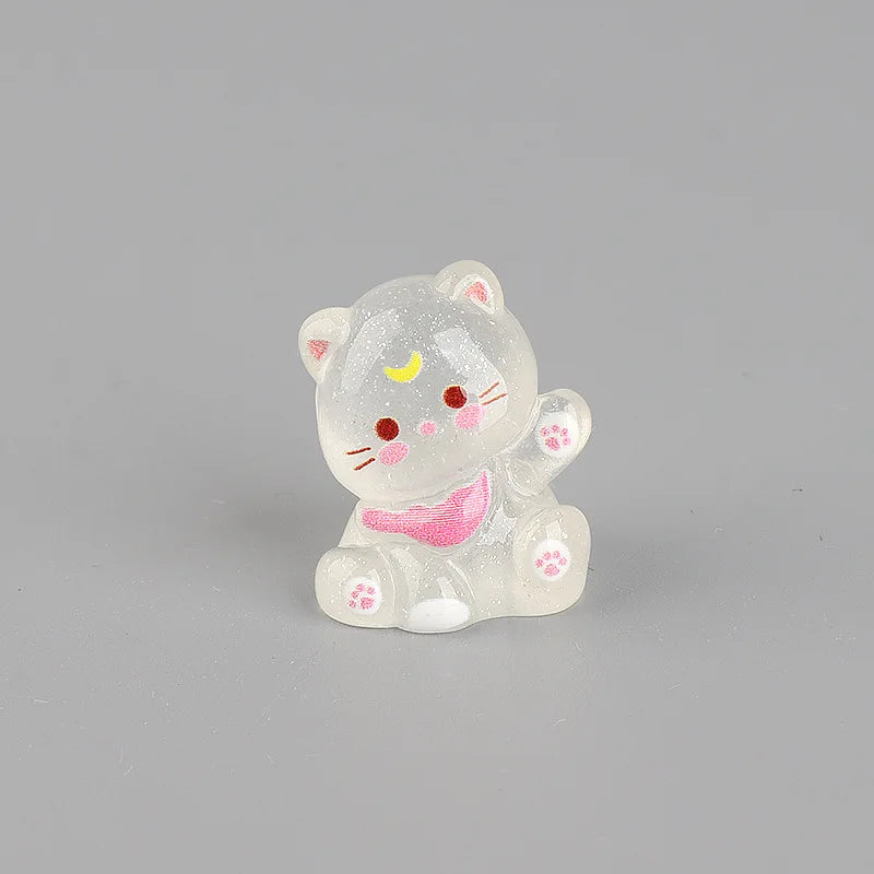 A small, translucent white resin figurine of a cat with pink accents and gold markings.