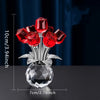 A glass vase filled with red crystal roses and silver leaves, displayed on a dark surface.