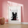 A framed photo of a couple embracing, featuring red playing card suits.