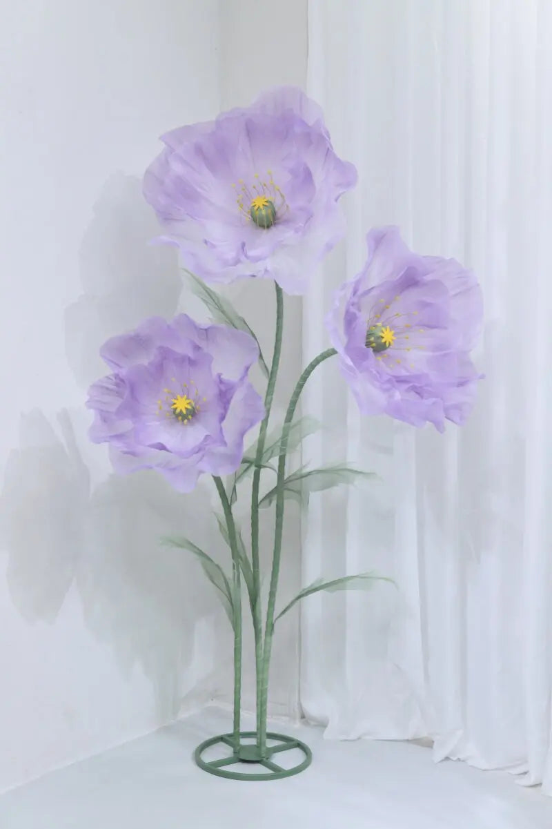 A large artificial silk purple poppy flower displayed on a green stand against a white background.