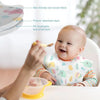A baby is eating with a spoon while wearing a skin-friendly non-woven fabric bib with a food catcher pocket.