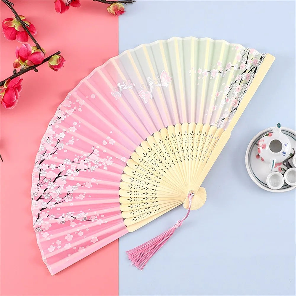 A pink and yellow vintage silk folding hand fan displayed on a light blue background.