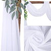 White chiffon wedding arch draping fabric panels with green foliage accents