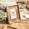 A wooden photo frame with a gold border displaying an orange fruit illustration on white paper.