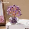 A crystal money tree ornament featuring purple amethyst clusters on a wooden branch displayed in a glass pot.