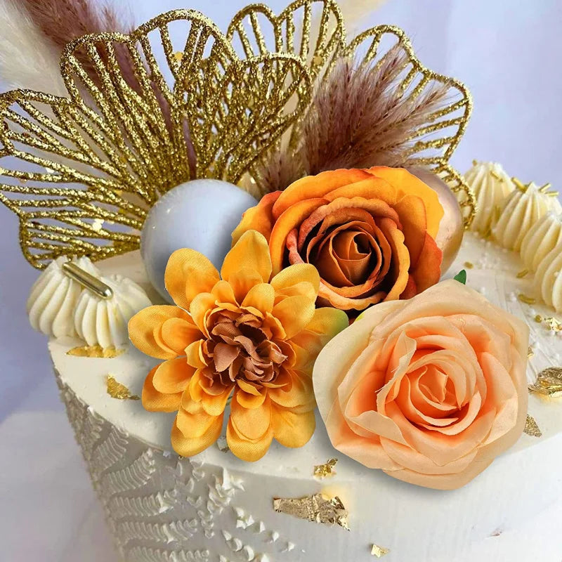 A cake decorated with orange and yellow roses, a golden palm leaf topper, and fluffy brown feathers.