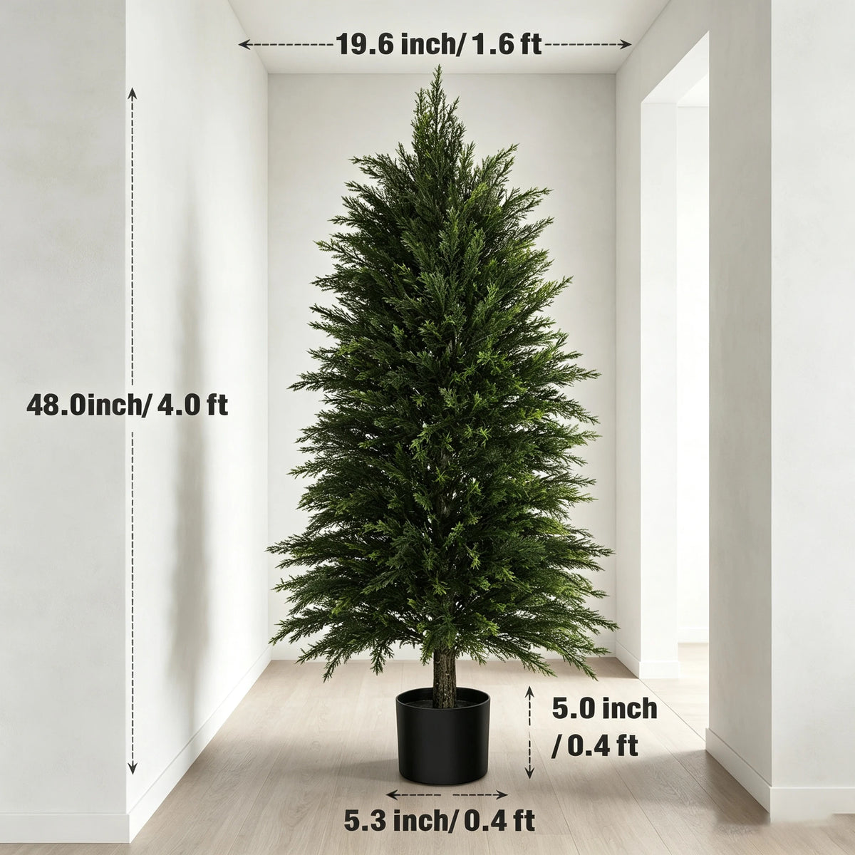 A tall artificial cedar topiary tree in a black pot displayed indoors against a white wall.