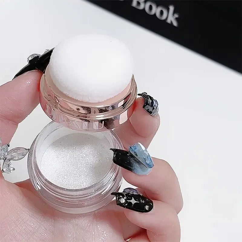 A hand holds a glass jar of Fairy Body Glitter Highlight Powder with a white dome and black glitter accents.