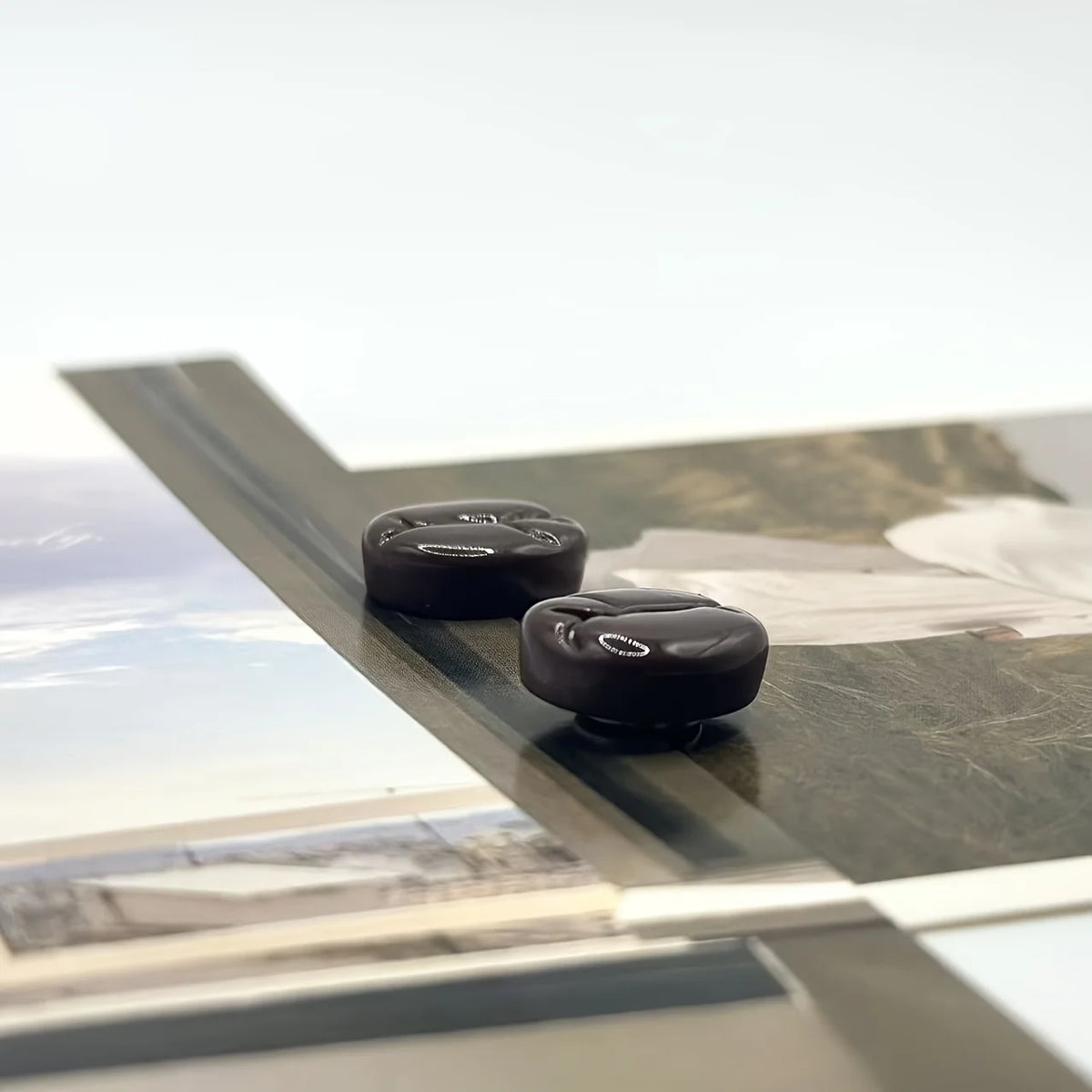 Magnets en forme de grains de café sombres posés sur une surface de verre.