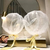 Two clear bobo balloons tied with yellow ribbon displayed on a gold stand for party decorations