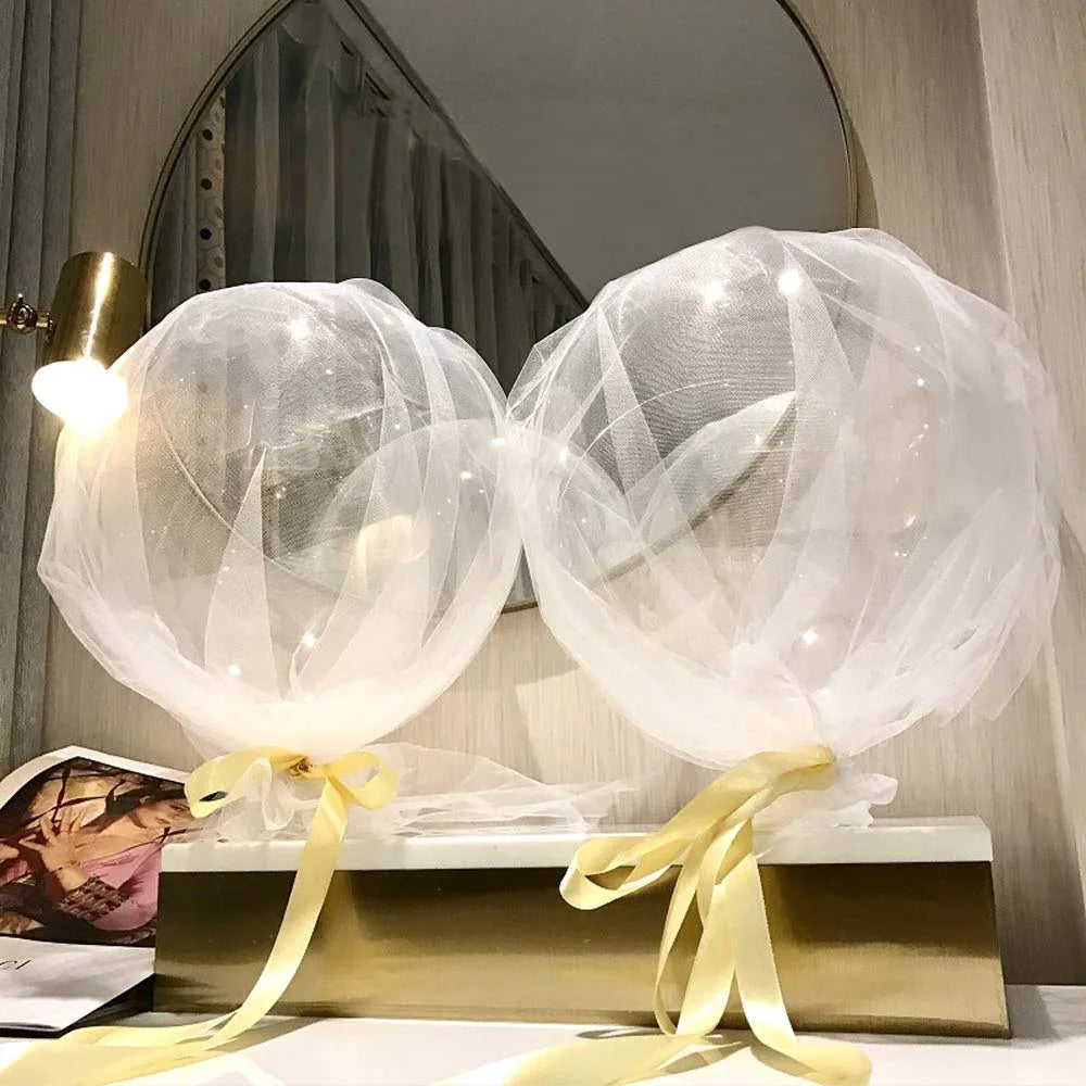 Two clear bobo balloons tied with yellow ribbon displayed on a gold stand for party decorations