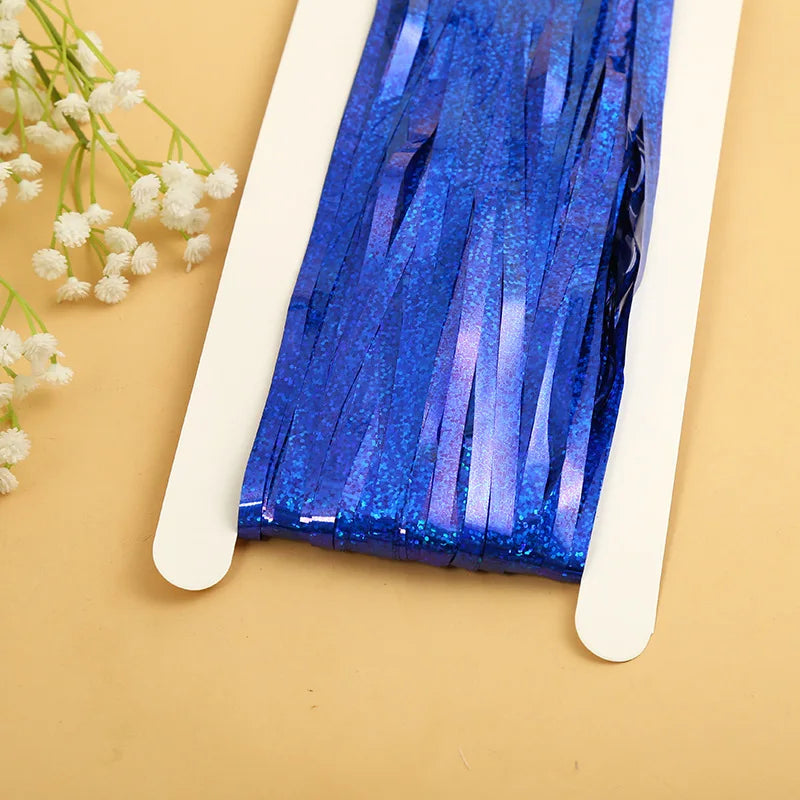 Blue metallic tinsel foil fringe curtain backdrop displayed on a white stand against a beige background.