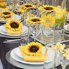 Yellow artificial sunflower heads displayed in various glass vases and on white plates for decoration