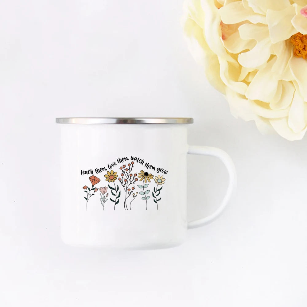 A white enamel mug featuring a line drawing of various flowers and the text teach them love them watch them grow.