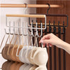 A hand is hanging light beige ceramic plates on a wall-mounted metal coat rack with multiple hooks.