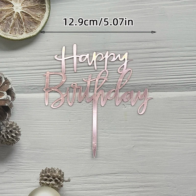A pink acrylic birthday cake topper with gold lettering spelling out Happy Birthday