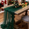 A wooden table draped with a sheer green fabric featuring beaded trim and festive holiday decorations.