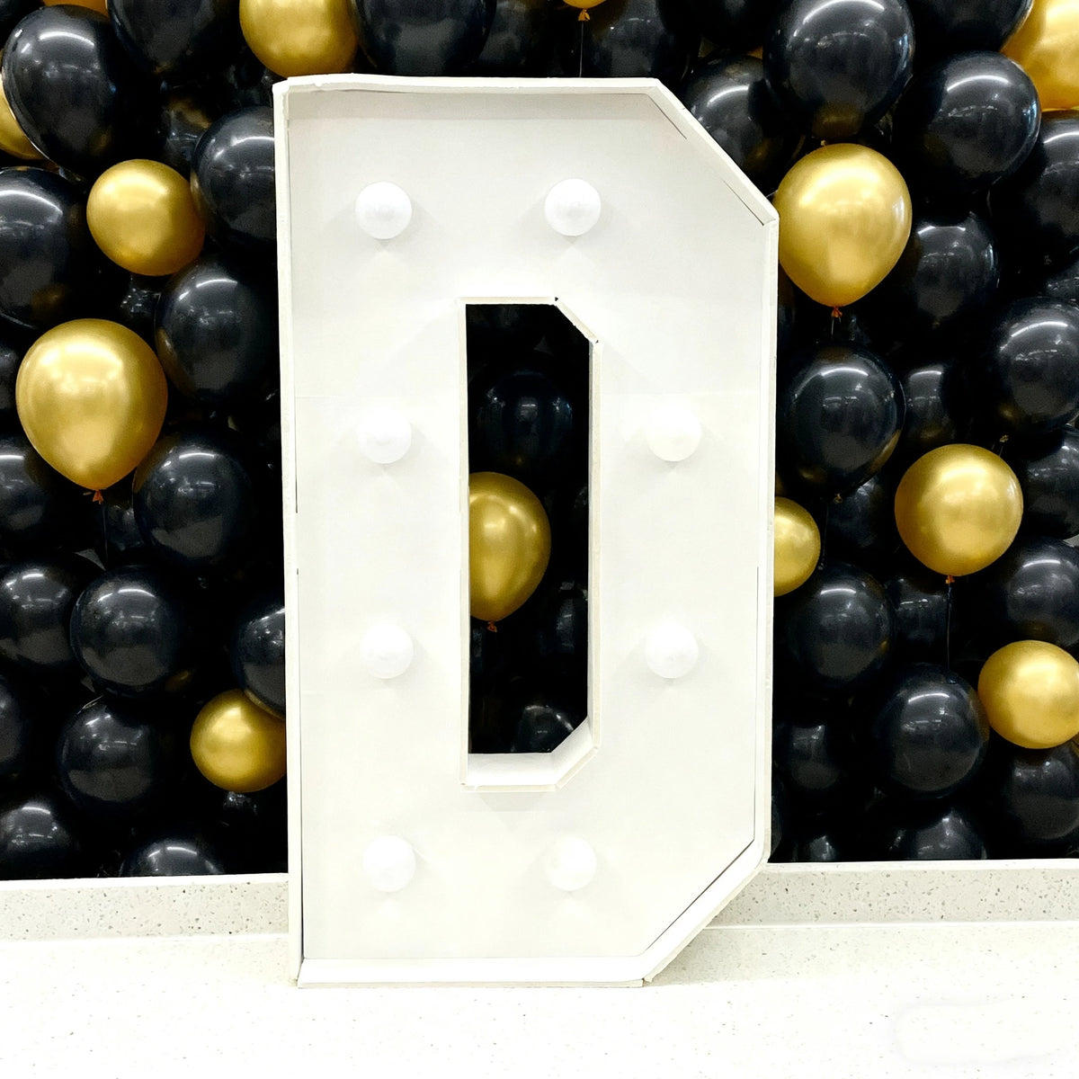 A large white marquee letter D made of balloons is displayed against a dark background.