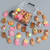 A collection of small capybara figures in various colors and textures displayed inside a clear plastic suitcase.
