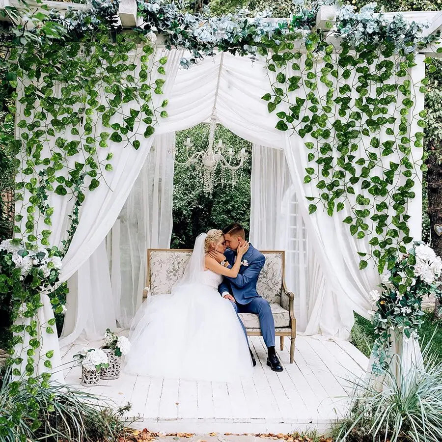 A bride and groom stand under a white archway decorated with greenery and flowers for a wedding photo.