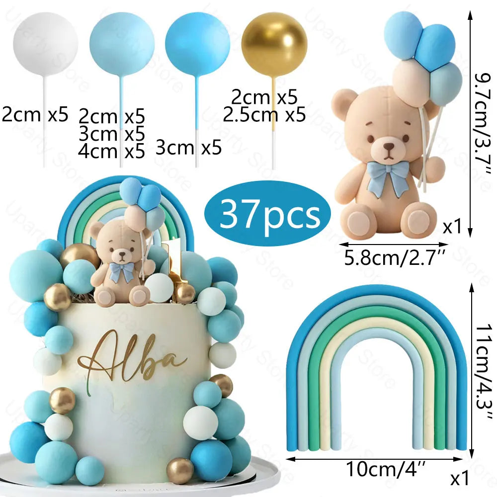 A cake decorated with blue and gold balloon toppers, including a bear figure and rainbow foam balls.