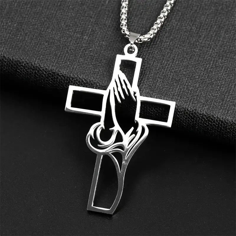 Silver hollow prayer hands cross pendant hanging from a chain on a black background
