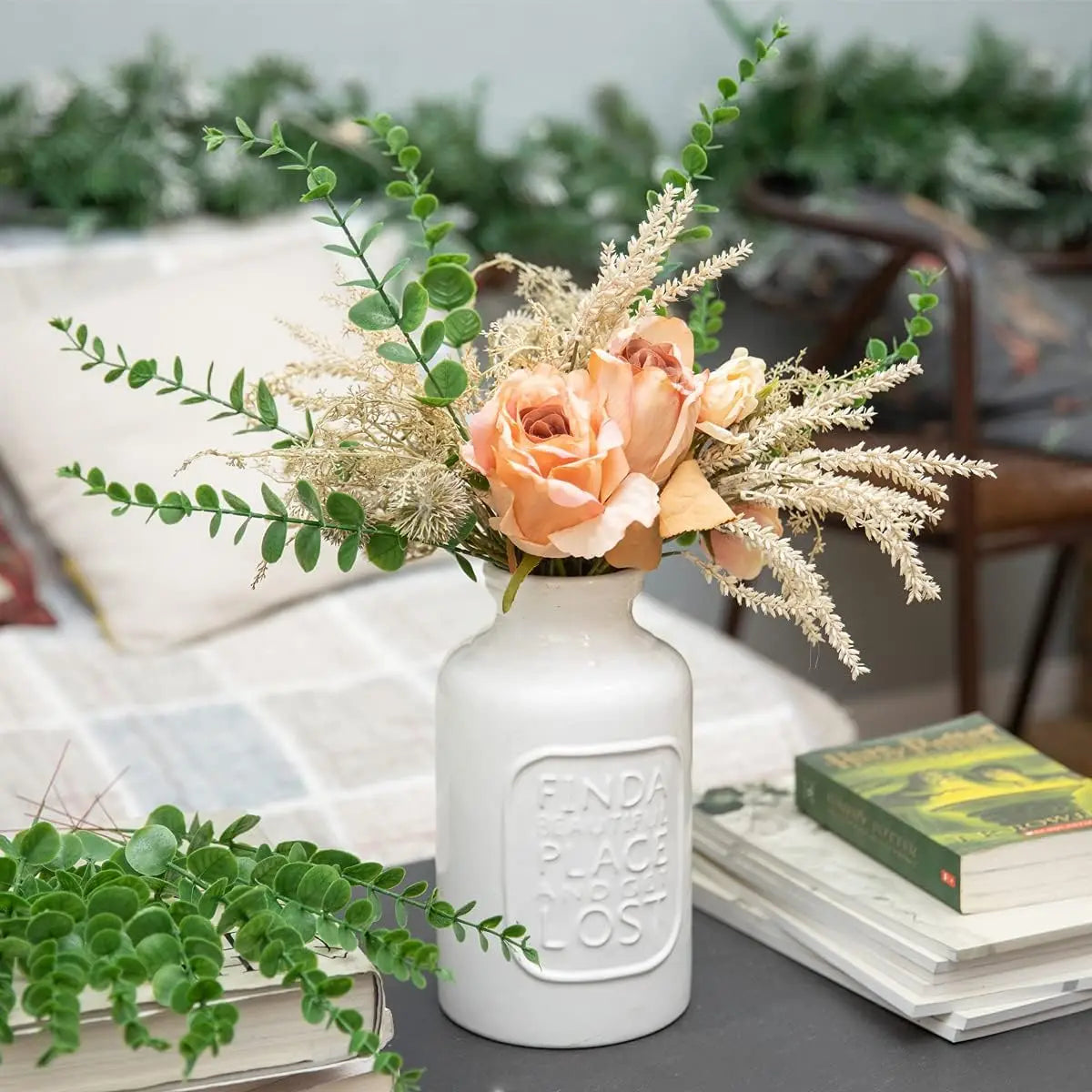 A bouquet of dried floral arrangements featuring peach roses and silvery green eucalyptus leaves in a white ceramic vase.
