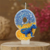 A birthday candle shaped like the number 9 featuring a blue dinosaur on an orange background.