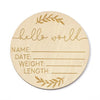 A round natural wood baby milestone disc with handwritten lines for name date weight and length measurements.