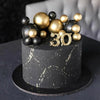 A dark cake decorated with gold and black ball toppers shaped like the number 30.