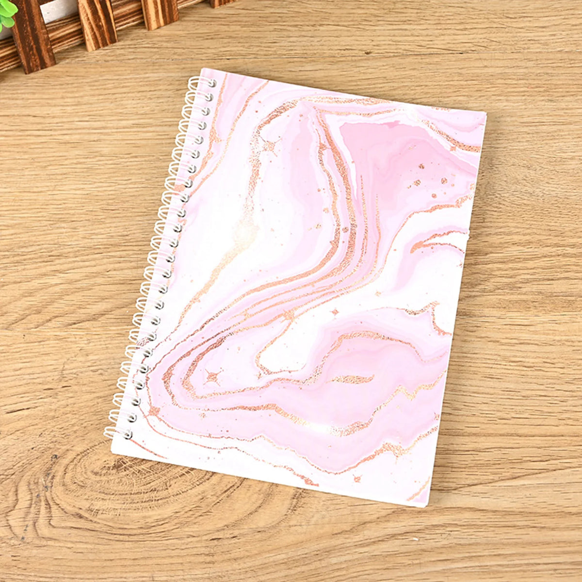 A pink marble patterned reusable sticker collecting album with a spiral binding lying on a wooden surface.