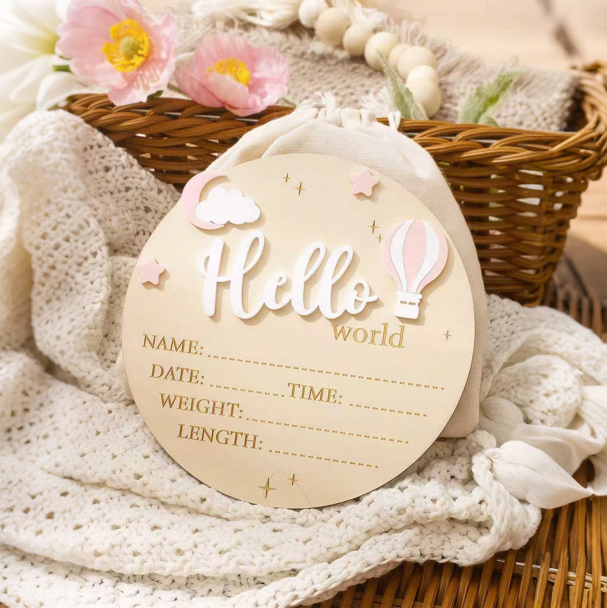 A round light pink newborn birth announcement sign with a cloud and balloon design resting on a white knitted fabric in a wic