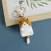 A handcrafted crochet cat keychain pendant with orange and white fur, attached to a gold ring.